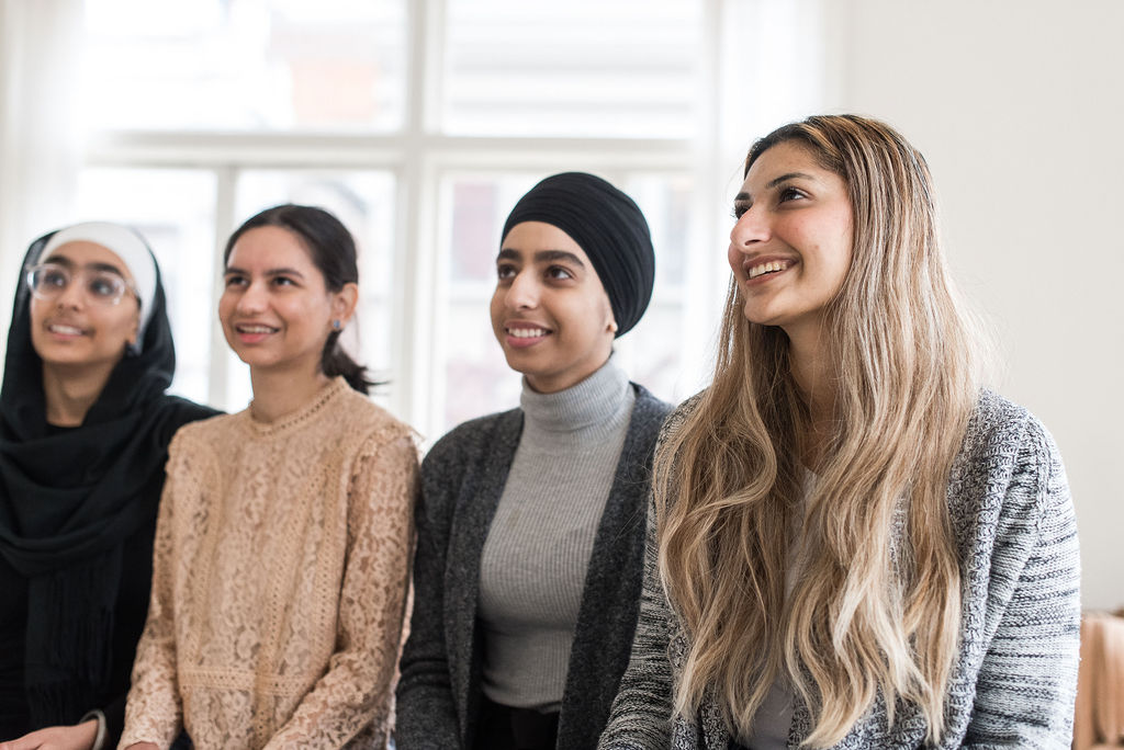 Four youth site in a line in front of a window